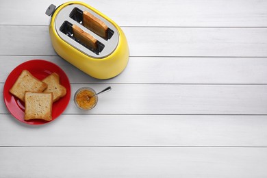 Yellow toaster with roasted bread and jam on white wooden table, flat lay. Space for text