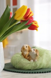 Photo of Easter decorations. Bouquet of tulips and bunny figures on table indoors, closeup