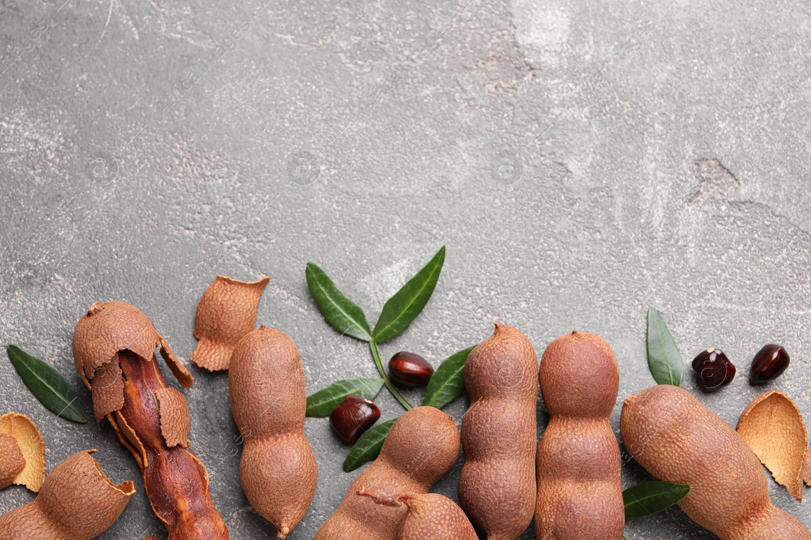 Photo of Ripe tamarinds and fresh leaves on grey table, flat lay. Space for text