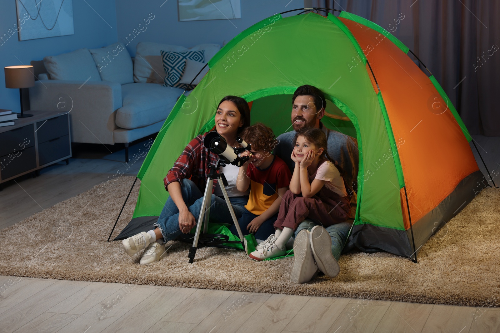 Photo of Happy family using telescope to look at stars while sitting in camping tent indoors