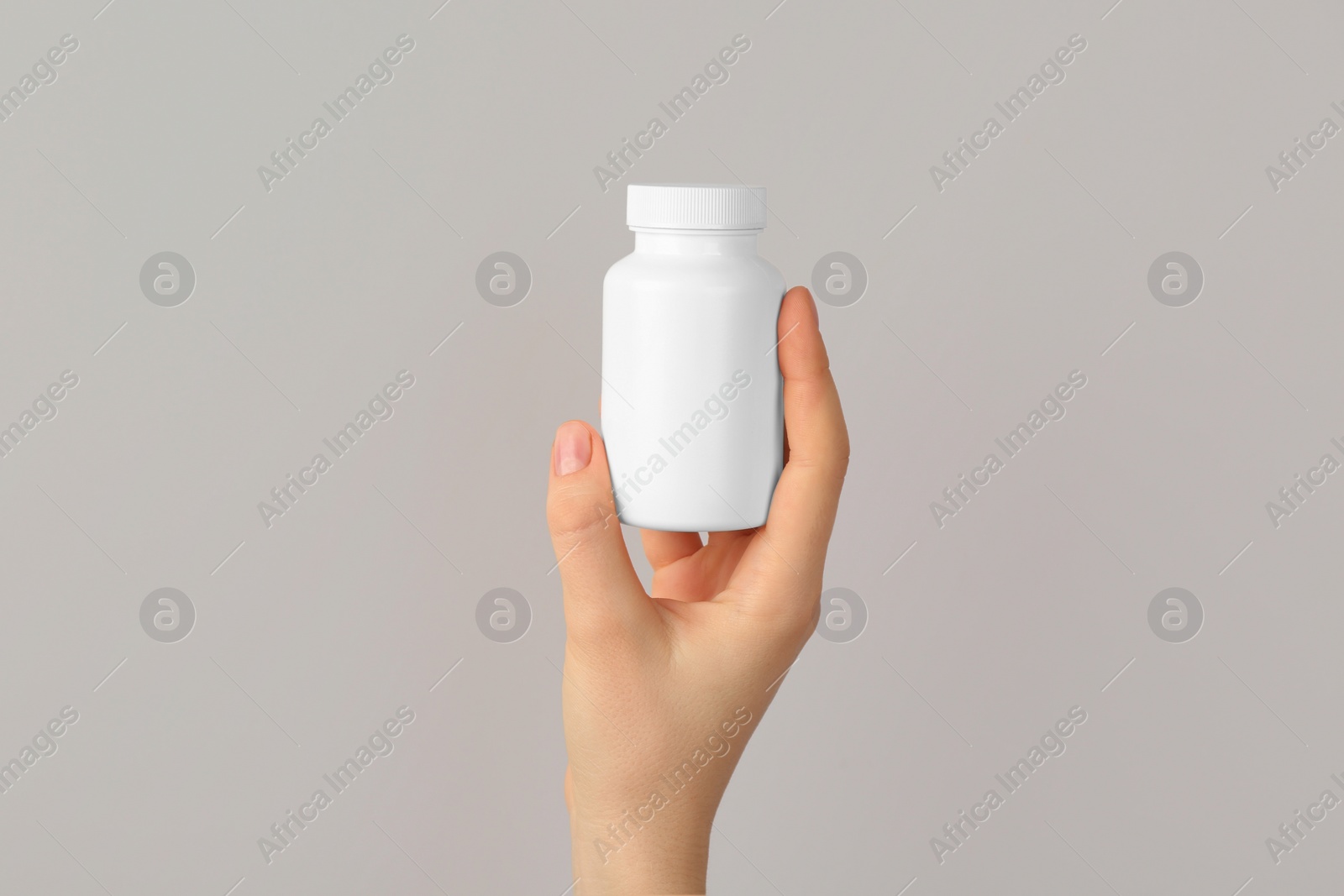 Photo of Woman holding blank white jar of vitamins on light grey background, closeup. Space for text