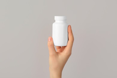 Photo of Woman holding blank white jar of vitamins on light grey background, closeup. Space for text