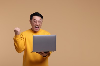 Emotional man with laptop on beige background, space for text