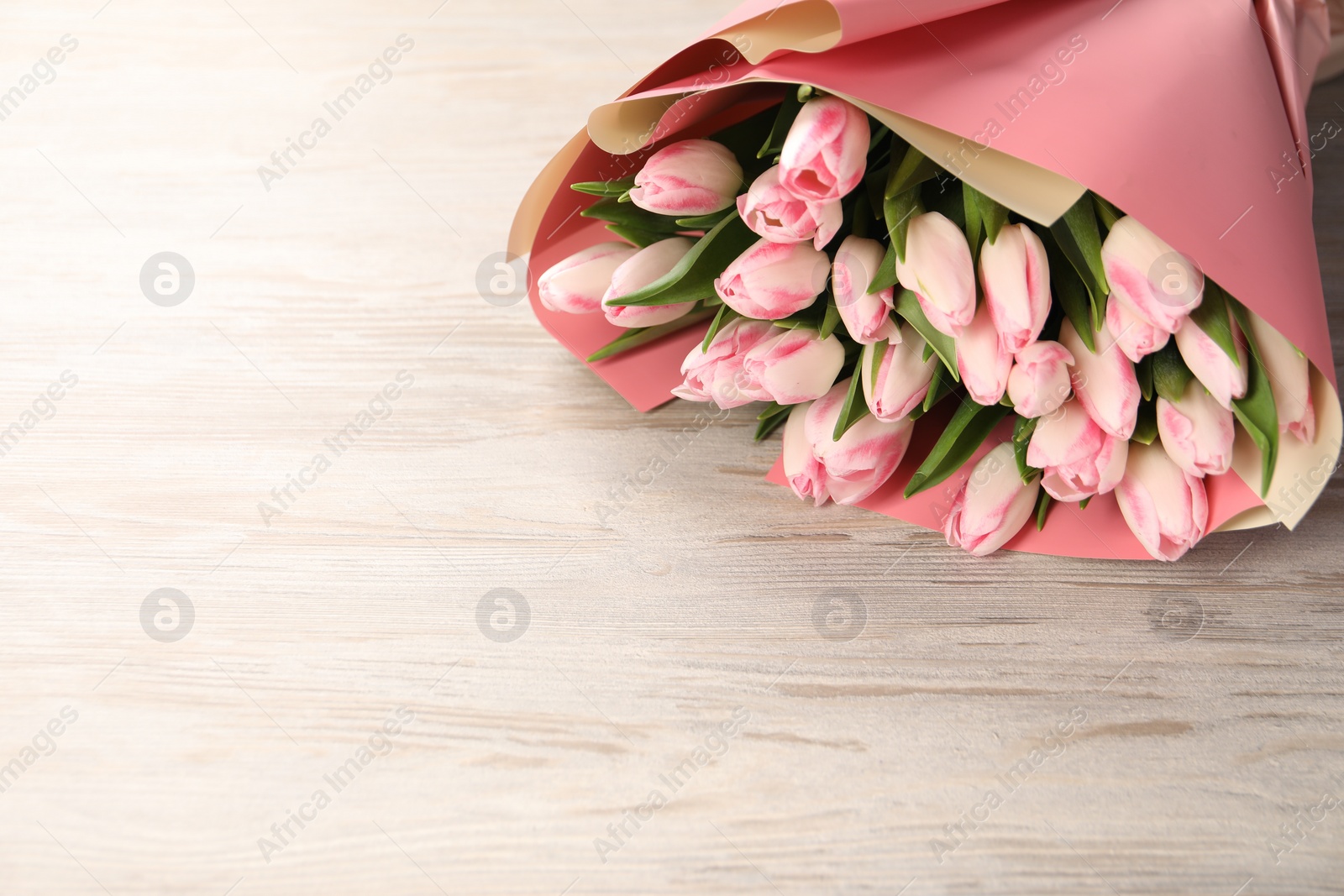 Photo of Beautiful bouquet of fresh pink tulips on light wooden table. Space for text