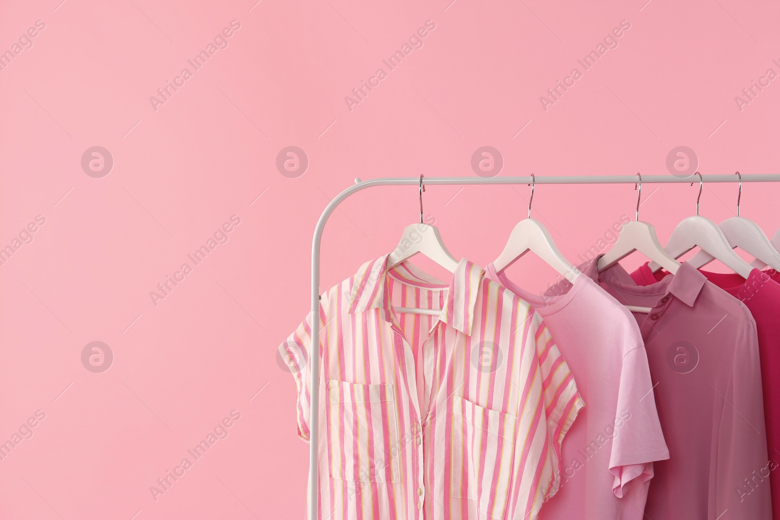 Photo of Rack with different stylish women's clothes on pink background. Space for text