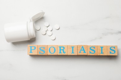Photo of Word Psoriasis made of wooden cubes with letters and pills on white marble table, flat lay
