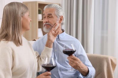 Photo of Affectionate senior couple with glasses of wine on sofa indoors