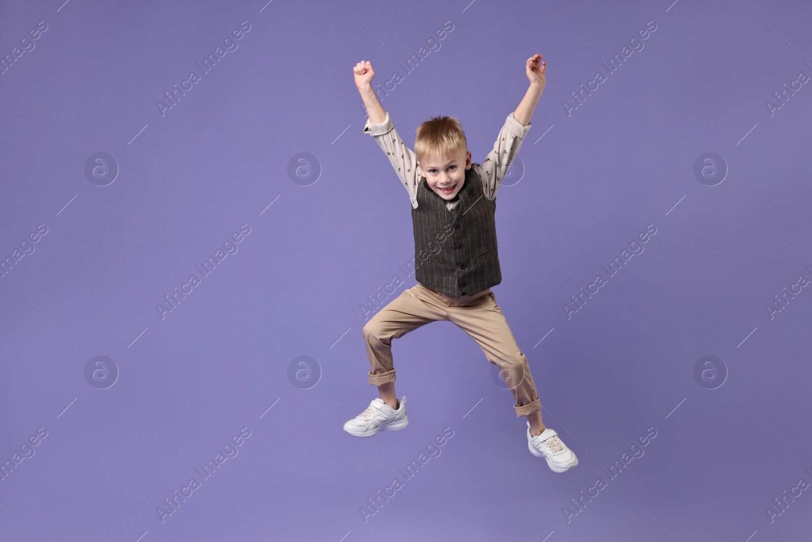 Photo of Happy little boy dancing on violet background. Space for text