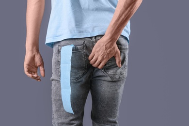 Photo of Man with toilet paper in pocket suffering from diarrhea on color background