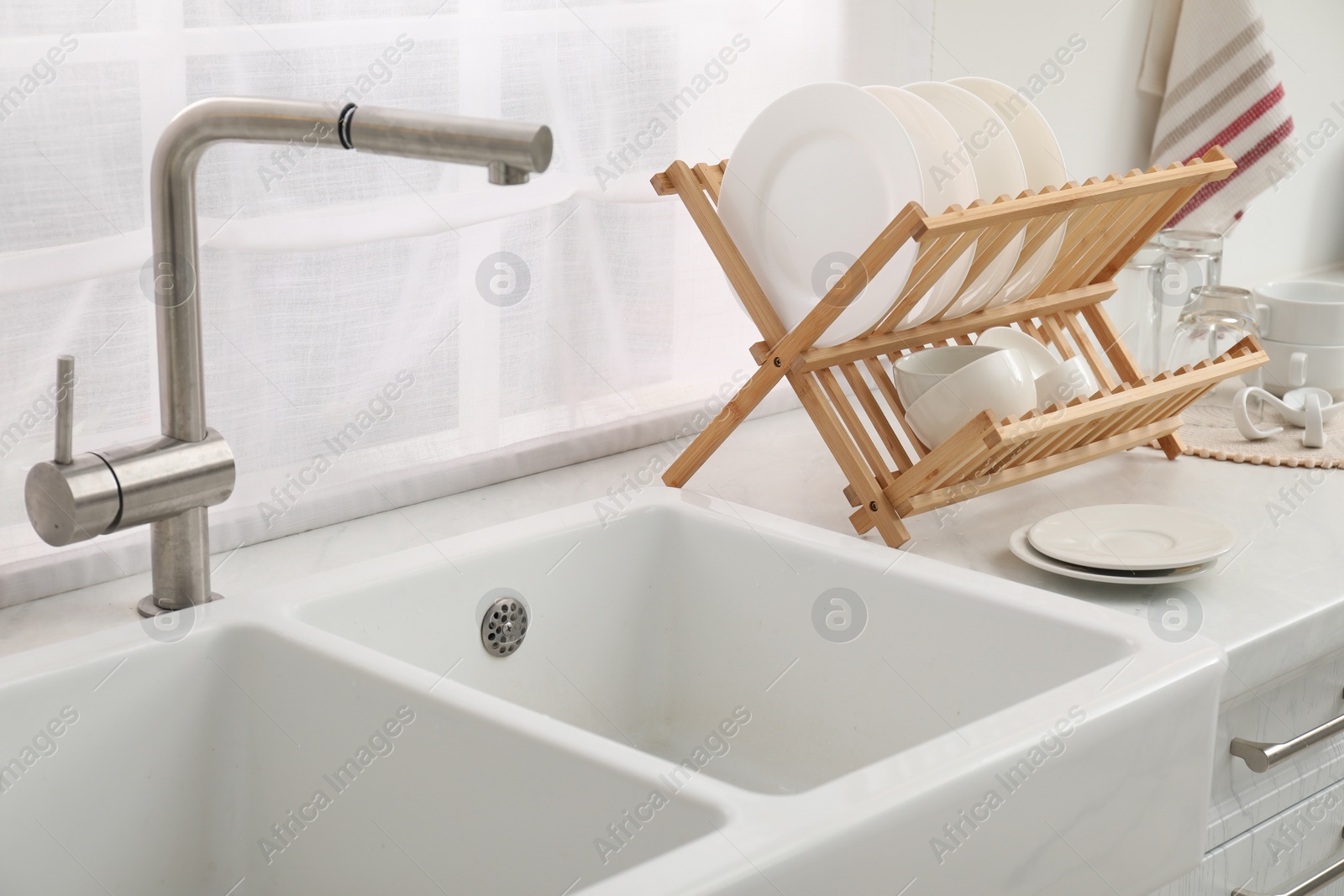 Photo of Drying rack with clean dishes on countertop near sink in kitchen