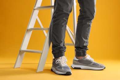 Photo of Man wearing stylish sneakers near white ladder on yellow background, closeup