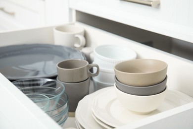 Open drawer of kitchen cabinet with different dishware, closeup