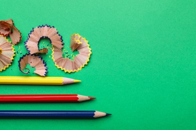 Photo of Color pencils and shavings on green background, flat lay. Space for text