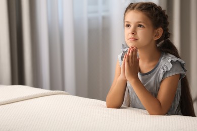 Photo of Cute little girl with hands clasped together saying bedtime prayer at home. Space for text