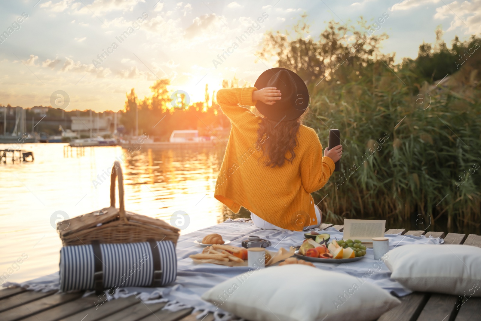 Photo of Young woman spending time on pier at picnic, back view