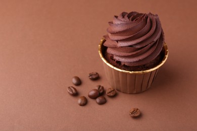 Photo of Delicious chocolate cupcake and coffee beans on brown background, closeup. Space for text