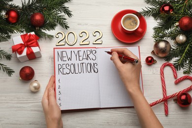 Photo of Woman filling list of New Year's resolutions in notebook on white wooden table, top view