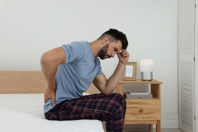 Photo of Man suffering from back pain after sleeping on uncomfortable mattress at home