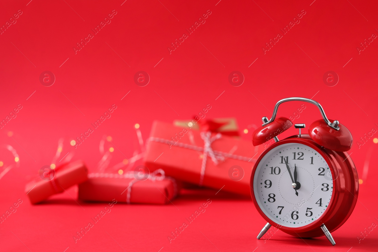 Photo of Alarm clock and gifts on red background, space for text. New Year countdown