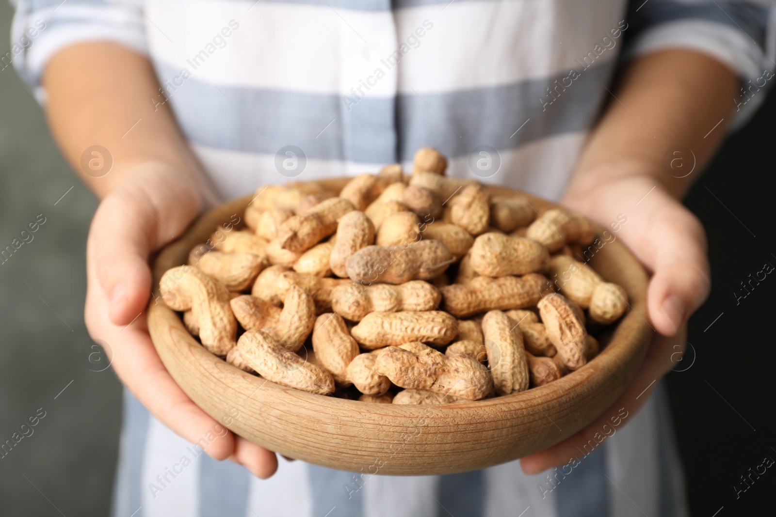 Photo of Woman holding bowl with raw peanuts in shell, closeup