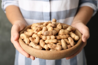 Photo of Woman holding bowl with raw peanuts in shell, closeup