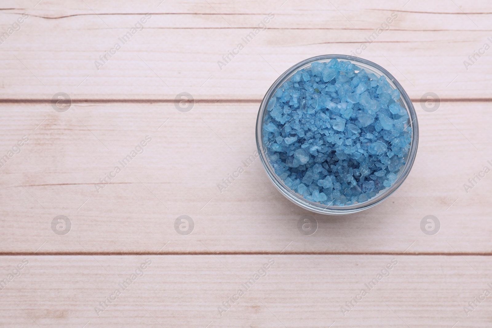 Photo of Blue sea salt in bowl on white wooden table, top view. Space for text