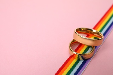 Photo of Wedding rings and rainbow ribbon on color background, space for text. Gay symbol