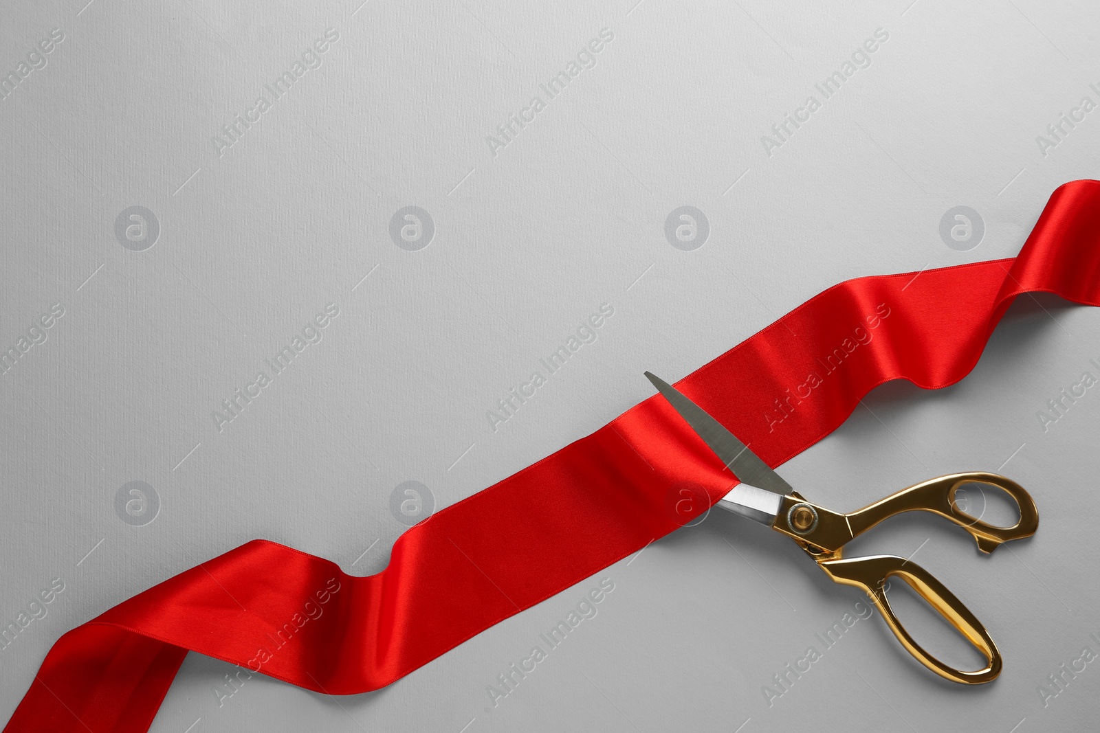 Photo of Red ribbon and scissors on light grey background, top view. Space for text