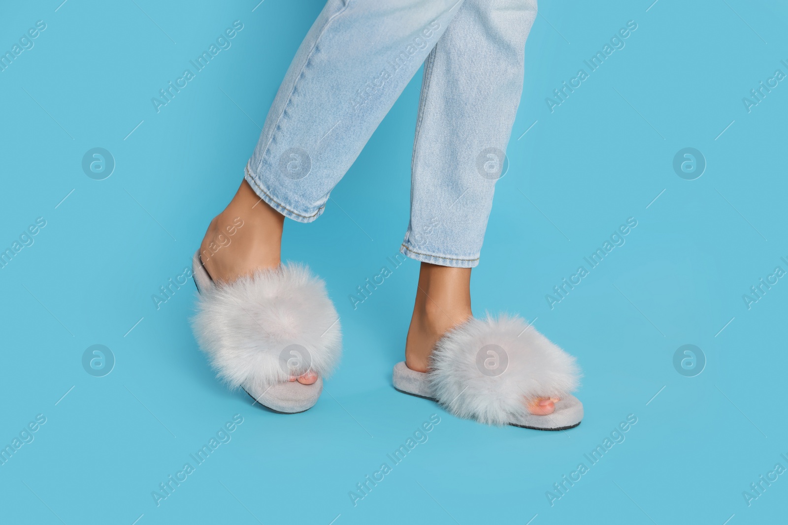 Photo of Woman in fluffy slippers on light blue background, closeup