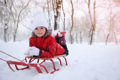 Photo of Cute little girl enjoying sleigh ride outdoors on winter day, space for text