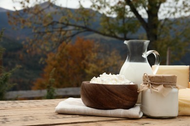 Photo of Tasty cottage cheese and other fresh dairy products on wooden table in mountains. Space for text