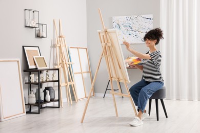 Photo of Young woman painting on easel with canvas in studio