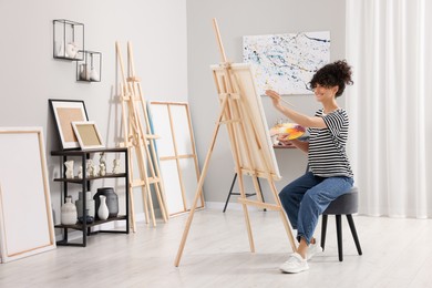 Young woman painting on easel with canvas in studio