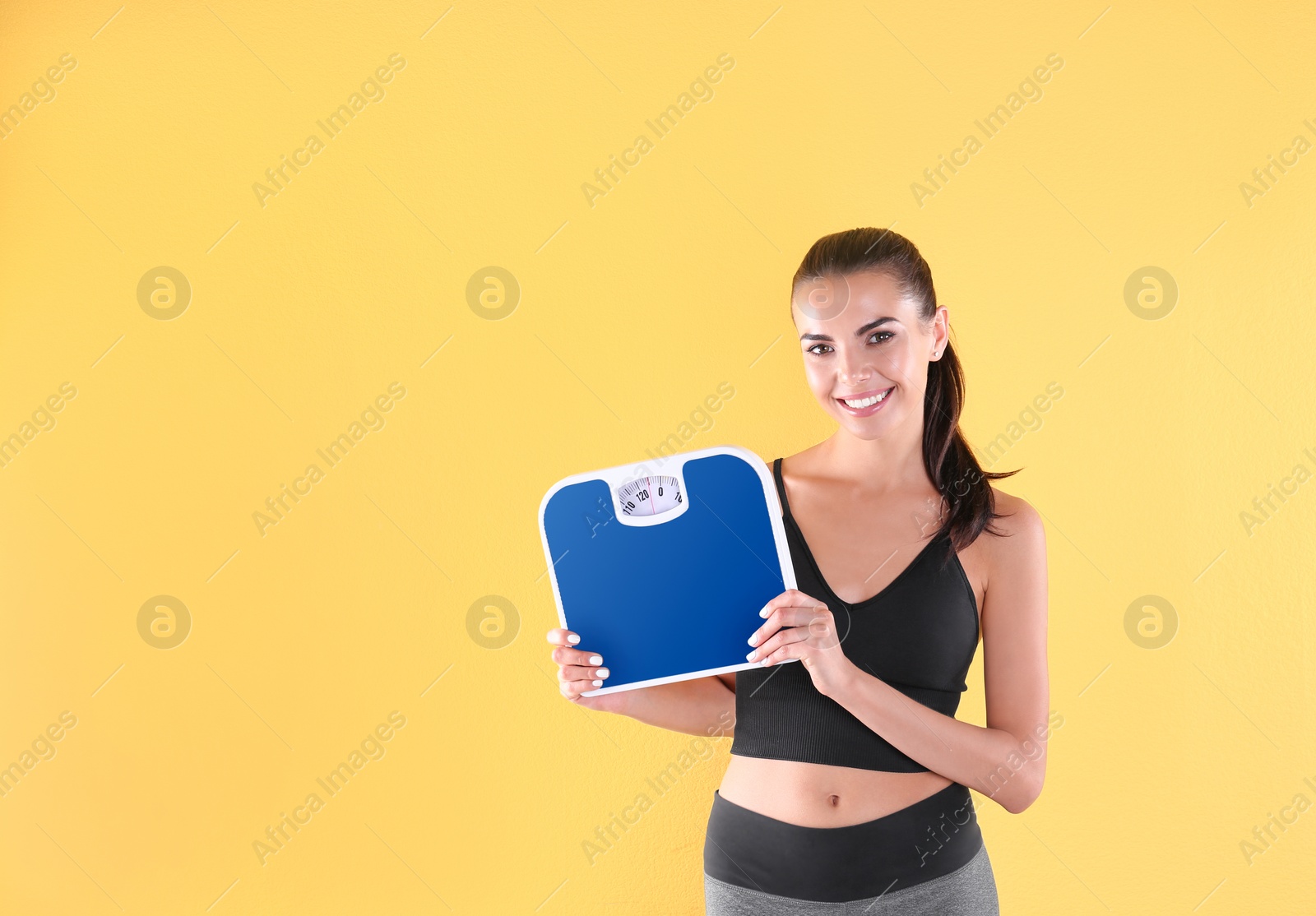 Photo of Happy young woman with scales on color background. Weight loss motivation