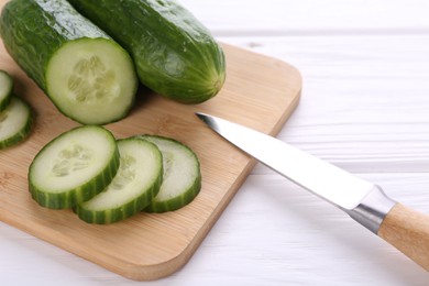 Photo of Cucumbers, knife and cutting board on white table, closeup