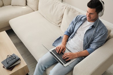 Photo of Man with laptop and headphones sitting on sofa at home