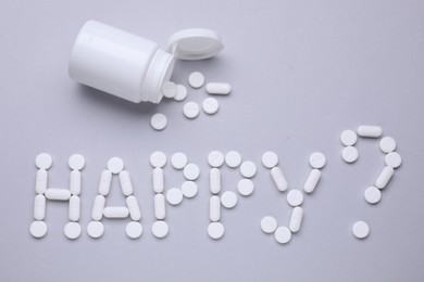 Photo of Question Happy made of antidepressants and medical bottle on grey background, flat lay