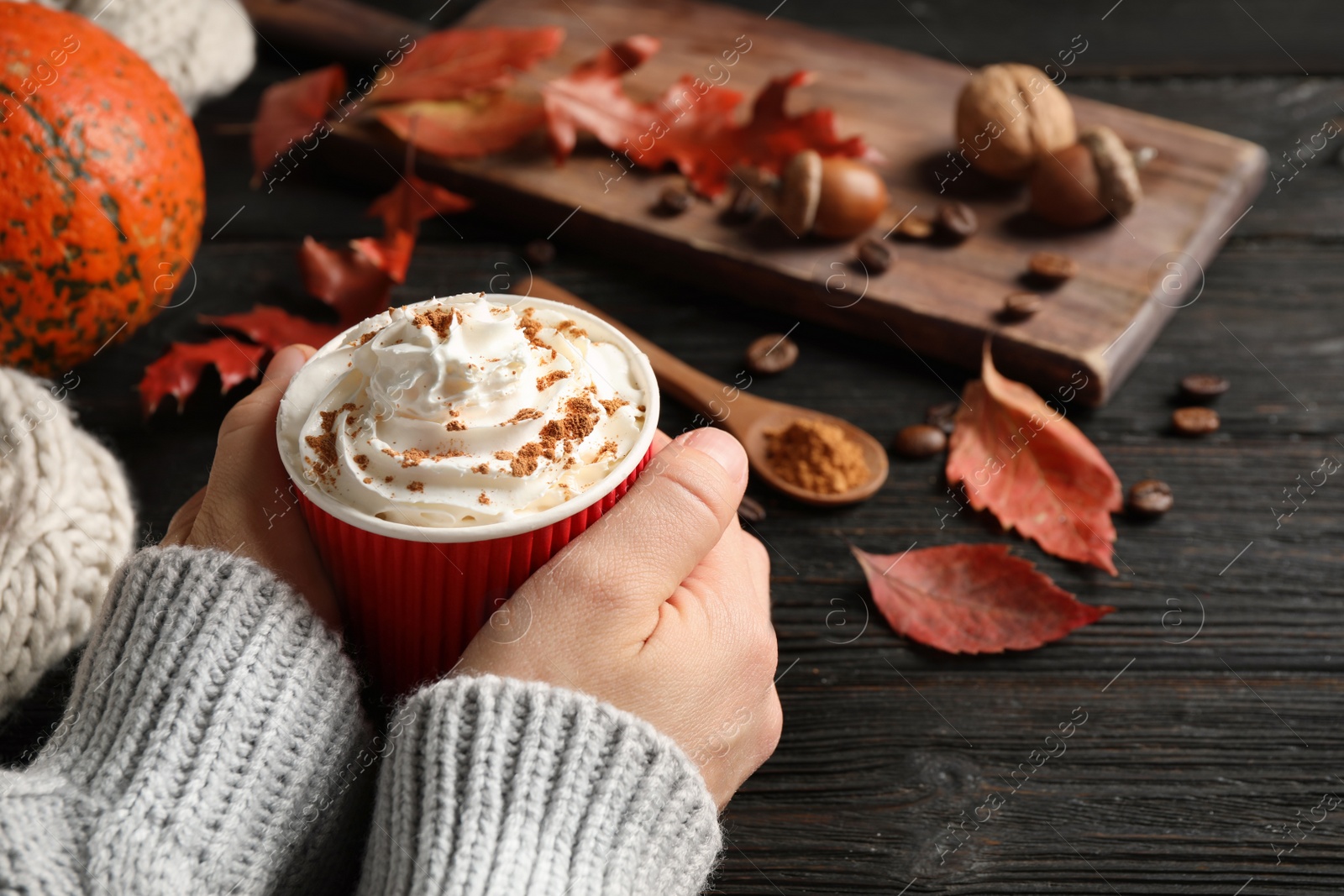 Photo of Woman holding paper cup with tasty pumpkin spice latte at black wooden table, closeup
