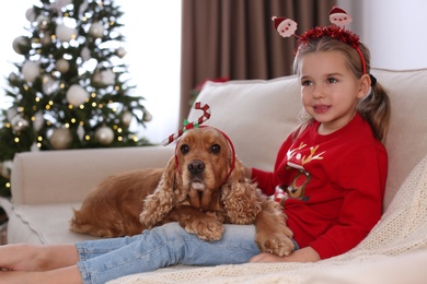 Photo of Cute little girl with English Cocker Spaniel in room decorated for Christmas