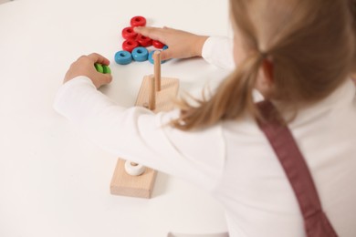 Photo of Little girl playing with stacking and counting game at white table indoors, closeup. Child's toy