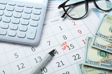 Photo of Calendar with date reminder about tax day, documents, money, pen, calculator and glasses, closeup