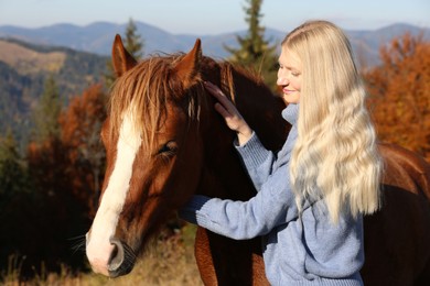 Photo of Young woman petting beautiful horse in mountains on sunny day