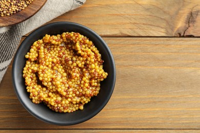 Fresh whole grain mustard in bowl on wooden table, top view. Space for text