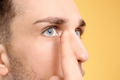 Photo of Young man putting contact lens in his eye on color background