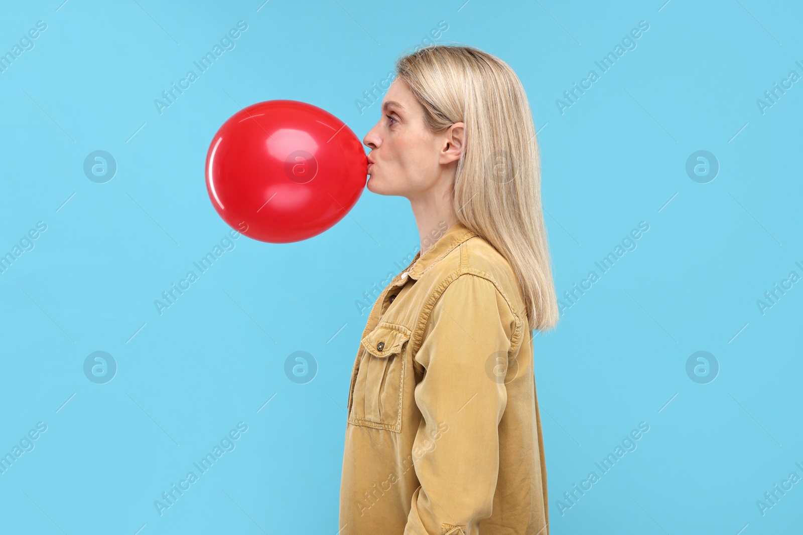 Photo of Woman blowing up balloon on light blue background