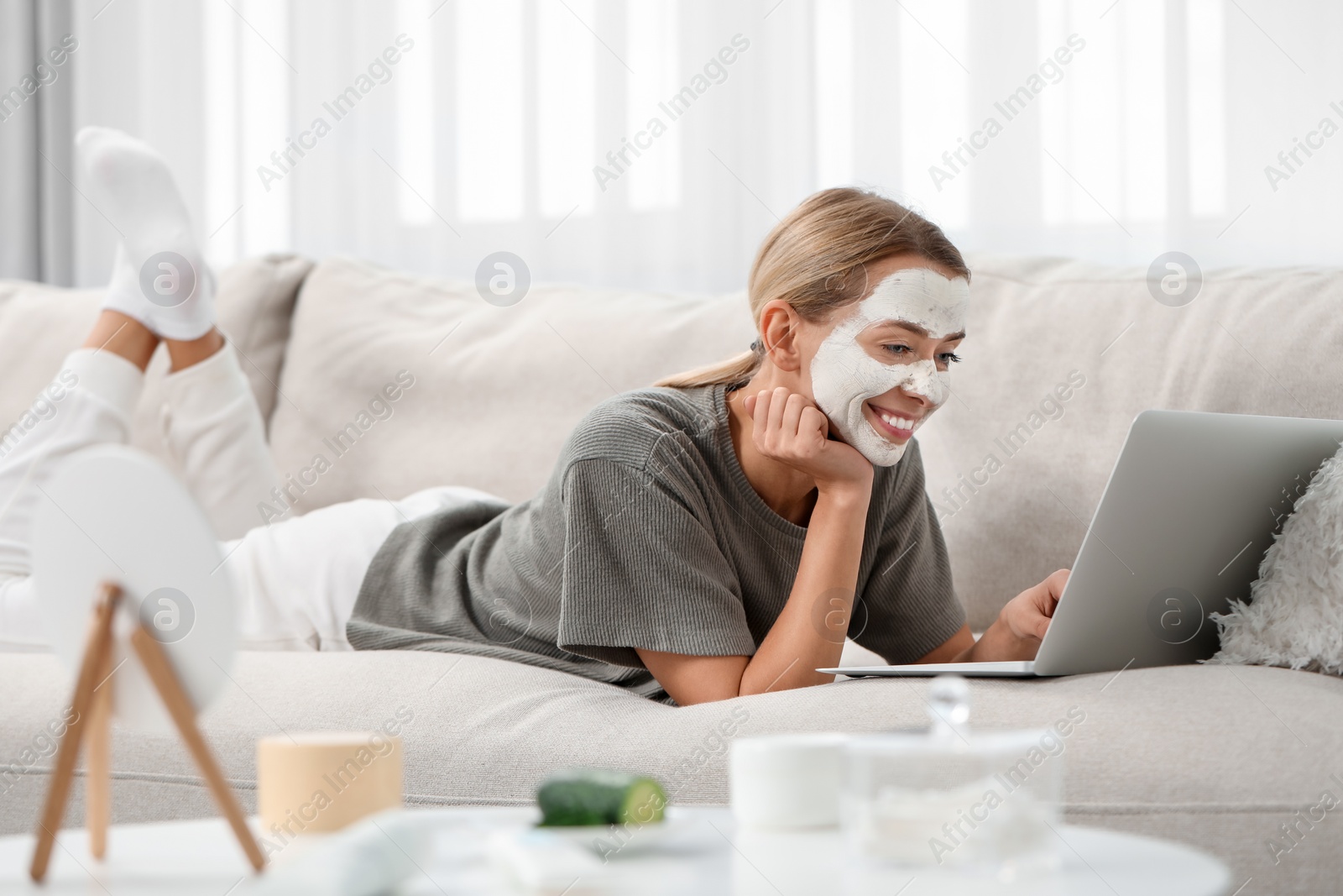 Photo of Young woman with face mask using laptop on sofa at home. Spa treatments