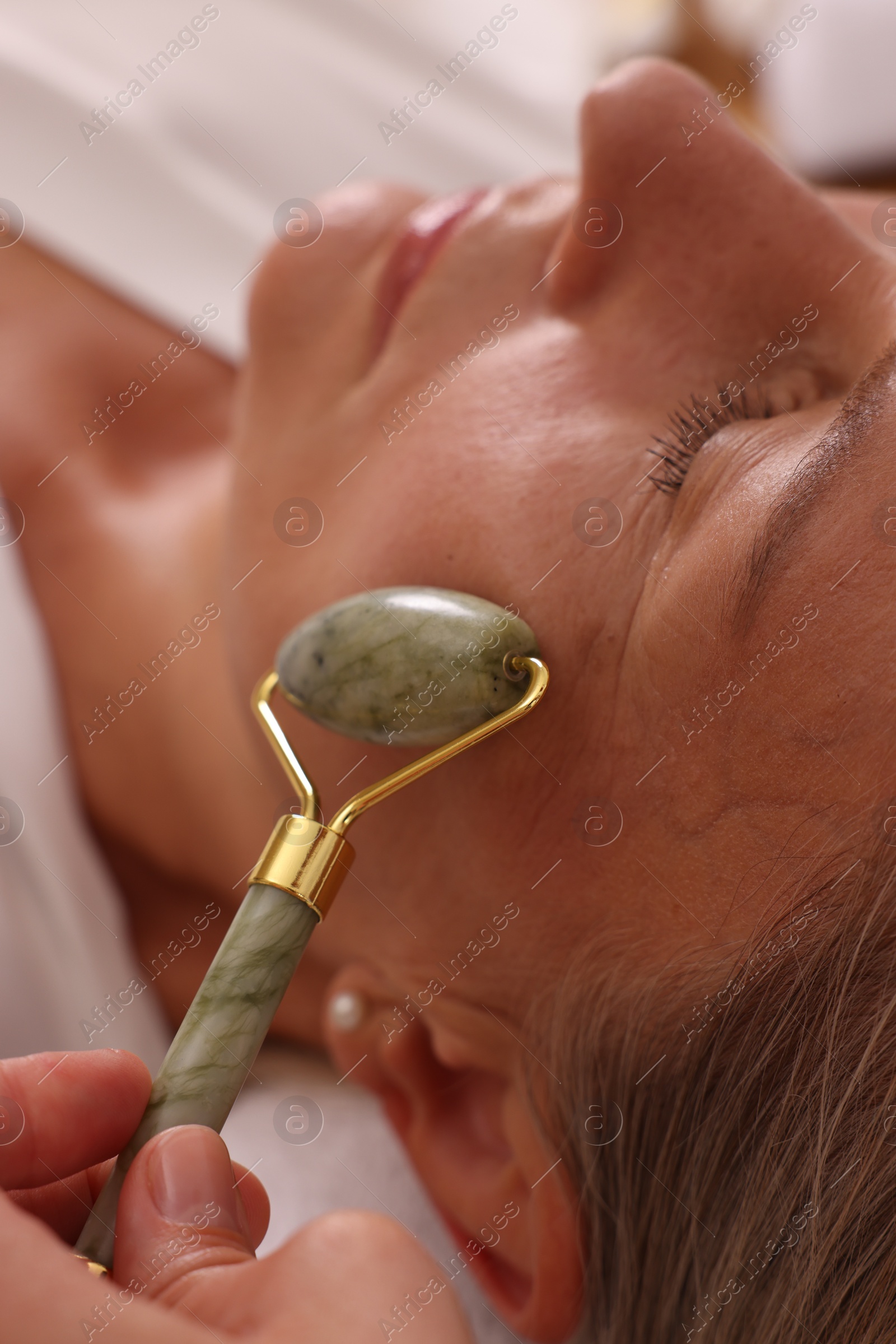 Photo of Woman receiving facial massage with jade roller in beauty salon, closeup