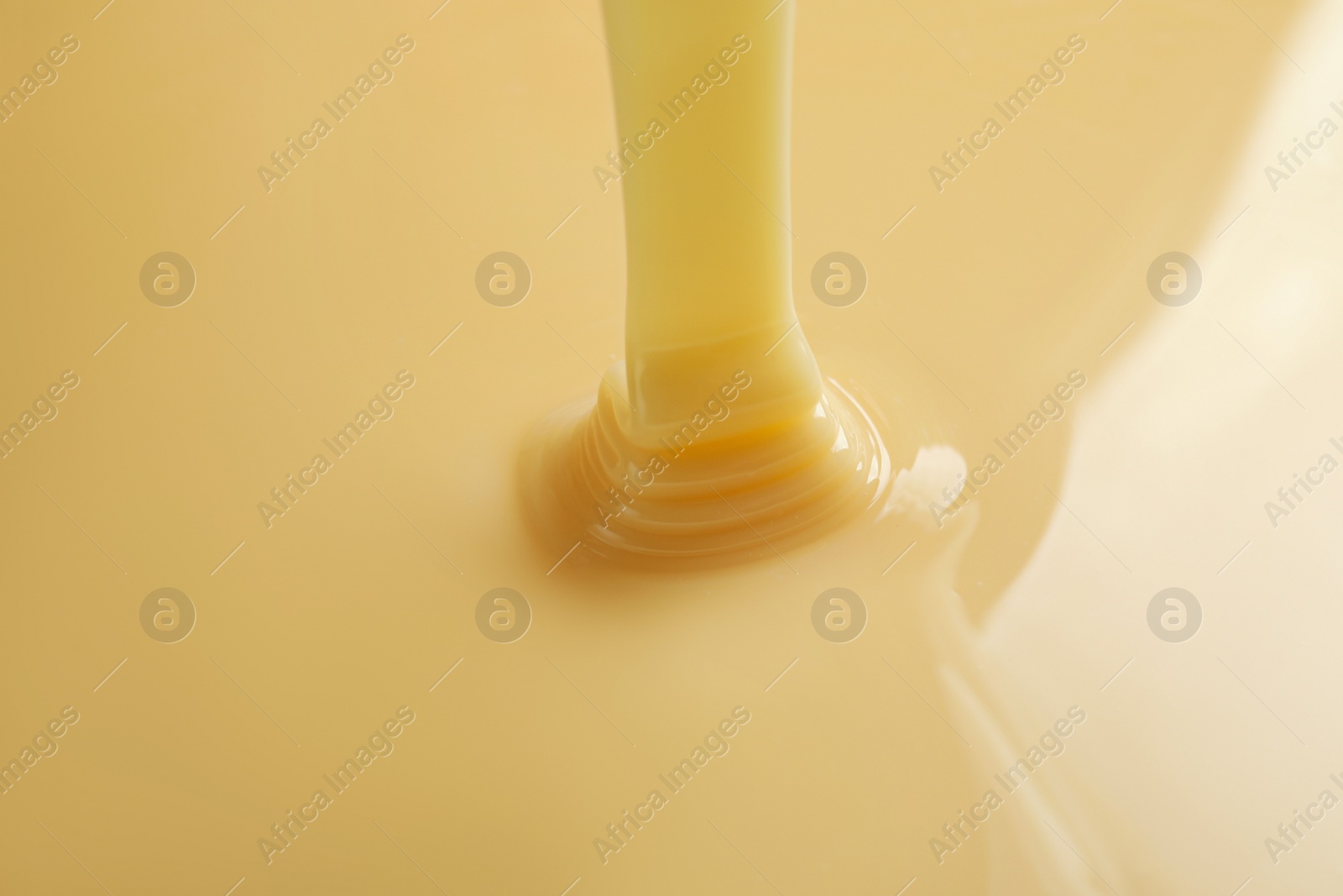 Photo of Tasty pouring condensed milk as background, closeup. Dairy product