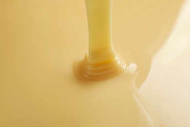 Tasty pouring condensed milk as background, closeup. Dairy product