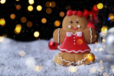 Gingerbread girl on snow against festive lights, closeup view with space for text. Bokeh effect